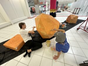 2 people paint a fake rock orange as part of the decor for the SLC WHITE PARTY
